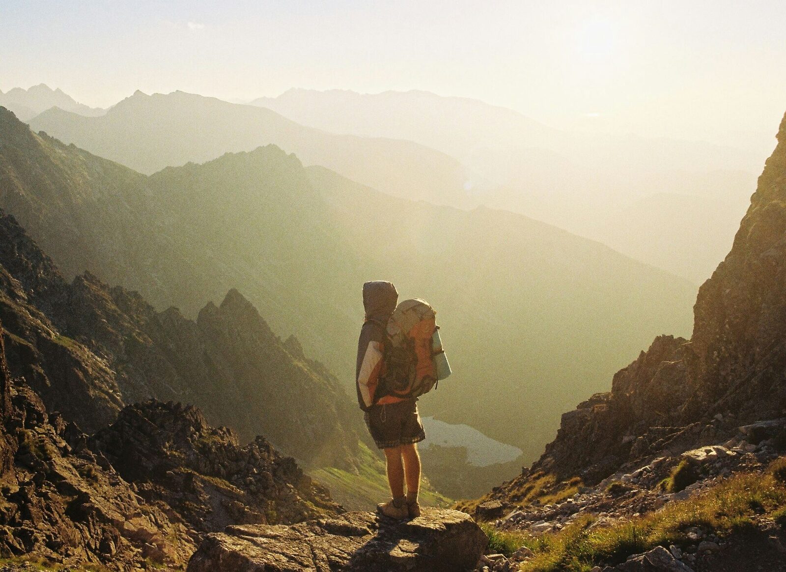 A lone hiker with a backpack standing on a ridge, looking out over a sunlit mountain valley