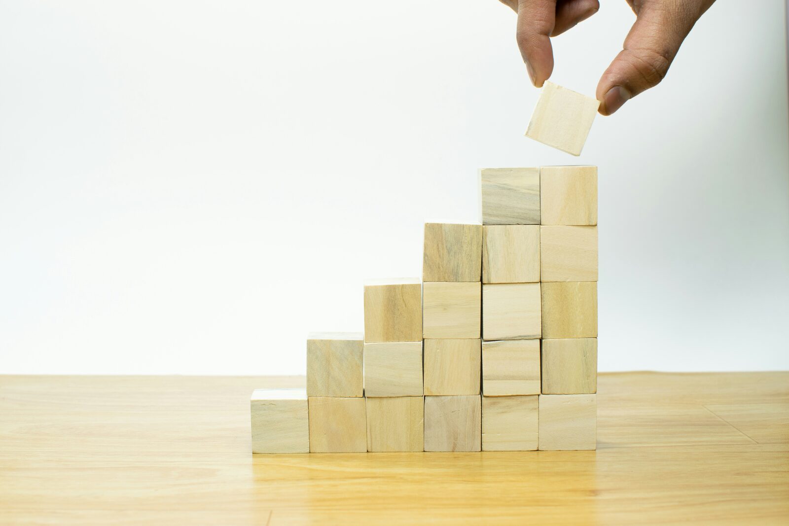 A hand placing the final wooden block on a rising staircase of stacked blocks